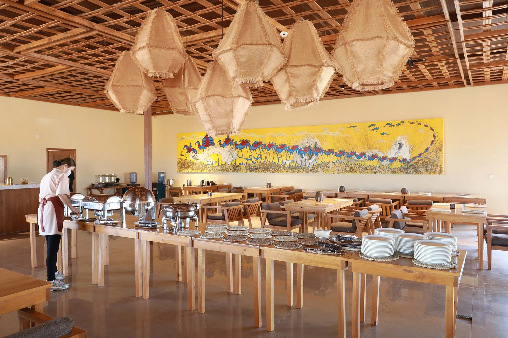 Tables with multiple pots inside a room decorated with art on the wall and hanging bamboo lamps.