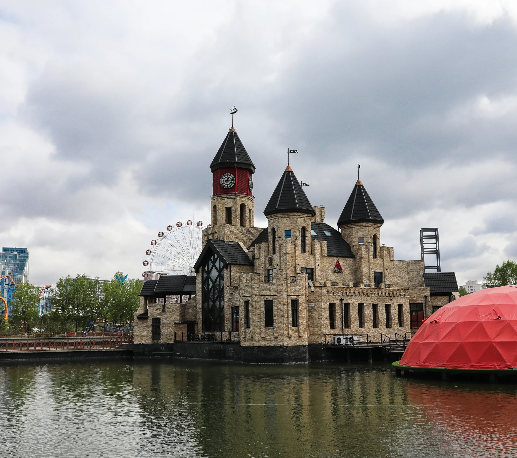 Castle-like building on water with towers, red dome, and Ferris wheel in background
