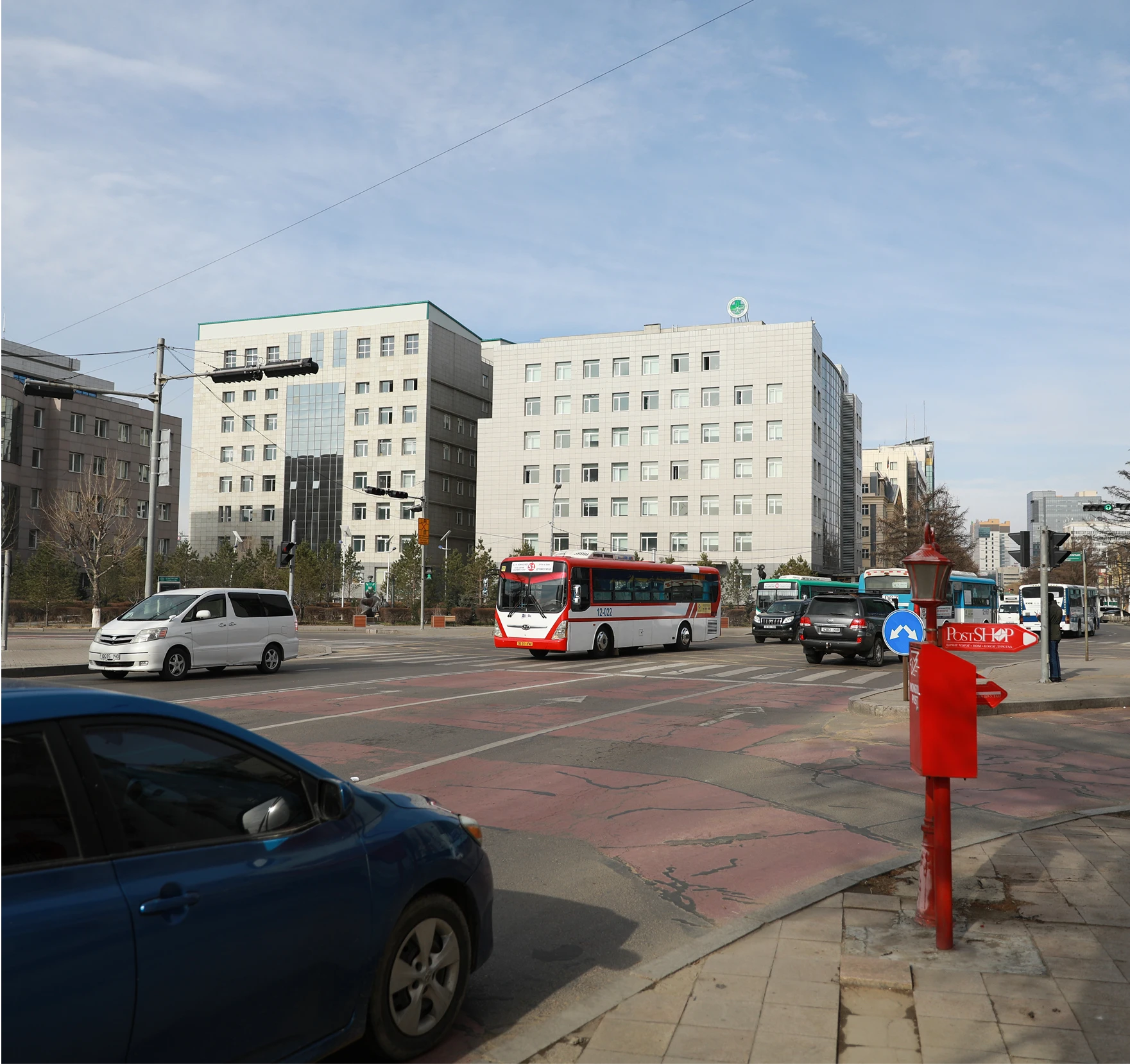 A road with buses, trucks and cars along with buildings in the background and a red post in the foreground.